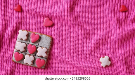 Noughts and crosses. A web banner for a website on the theme of love. Gingerbread on a pink sweater background. Horizontal Wallpaper