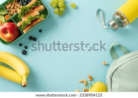 A nourishing school break scene from above, displaying a lunchbox with sandwiches accompanied by fruits, berries, water bottle and rucksack on blue isolated backdrop, perfect for text or advertising