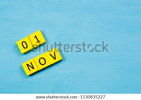NOV 1, yellow cube calendar on blue wooden surface with copy space