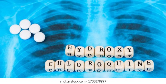 Novel Covid-19, Coronavirus. Infected Lungs Radiology Blue Image Background, With White Pills On It. Hydroxy Chloroquine Written With Wooden Letters.