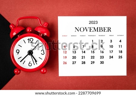 November 2023 Monthly calendar year with alarm clock on red and black background.