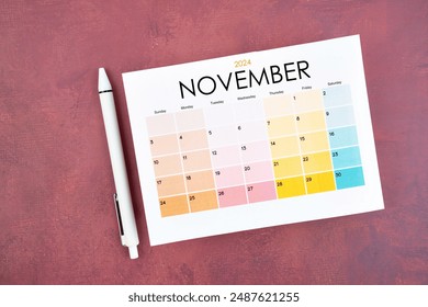 November 2024 calendar page and pen on red color retro background.