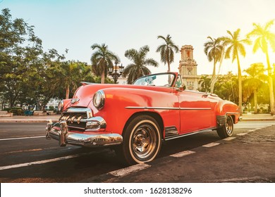 November 27, 2019, Havana, Cuba. Classic American Car Against The Background Of Palm Trees In The Bright Sun In The Evening In Havana Against The Background Of Colonial Architecture