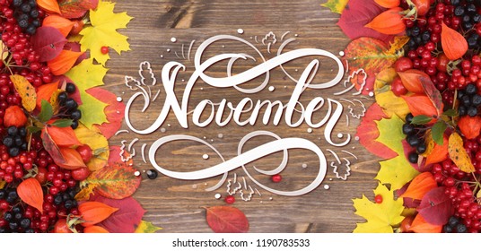 November hand lettering inscription. Bright red autumn leaves and berries frame composition on old wooden background. Great season texture with fall mood. Nature november background. 