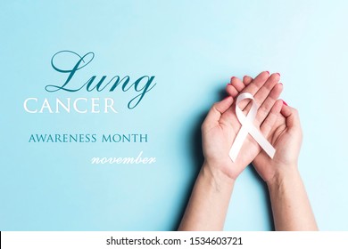 November lung cancer awareness month. Female hands holding white ribbon on a blue background. 