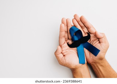 In November, men's health and Prostate cancer awareness take center stage. Man's hands embrace a light blue ribbon with a mustache on a blue background a symbol of support. - Powered by Shutterstock