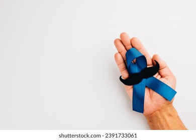 In November, show your support for men's health and Prostate cancer awareness. Hands hold a light blue ribbon with a mustache on a blue background a symbol of unity. - Powered by Shutterstock