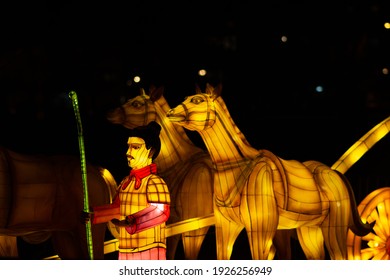 Novi Sad, Serbia – February 26, 2021: The Chinese Lantern Festival At The Limanski Park. A Man With A Red Scarf, Holding A Bamboo Stick, Is Standing Next To A Carriage Pulled By Horses; A Detail.