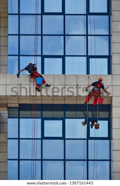 Novi Sad, Serbia,\
May 17th 2015. - Window cleaners working on building , cleaning the\
facade hanging on the rope