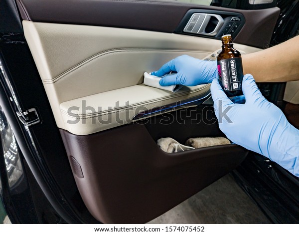 Novosibirsk, Russia - 08.01.2018: Applying a\
nano-ceramic coating for interior Ceramic Pro Leather 9h and Light\
on the car door white upholstery by a worker with a sponge and\
chemical\
composition