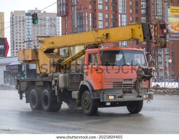 Novosibirsk, Russia - April 05 2021: orange\
metallic color russian lift crane truck КС 55713-1 old classic car\
on chassis 80s 90s 2000s KamAZ 55111-15 local cargo truck drive\
dirty city urban\
street