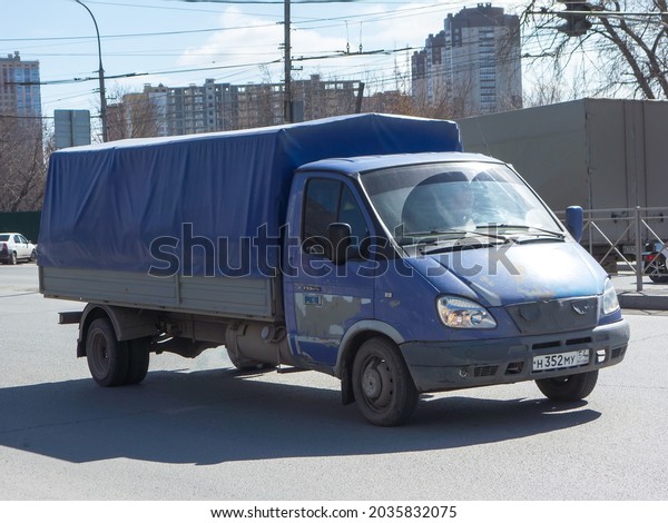Novosibirsk, Russia - April 20 2021: purple blue\
metallic color russian small flatbed awning covered old 2000s car\
GAZ Gazelle long base, local quick delivery cargo truck driving\
sunny urban street