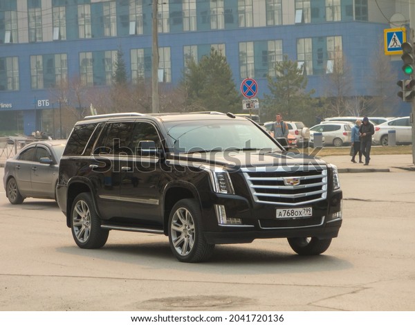 Novosibirsk, Russia - april 27 2021: private awd\
all-wheel drive black metallic color north american new car SUV\
Cadillac Escalade, USDM US-spec crossover exported made in USA\
driving on urban street\
