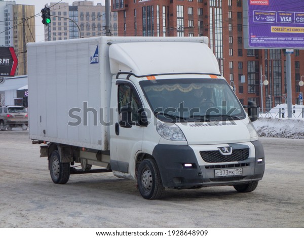 Novosibirsk, Russia - february 09 2021: white metallic\
color franch box car chassis light new Peugeot Boxer, popular small\
cargo shiping mini truck drive on winter snow unclean unpaved urban\
street 