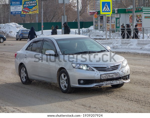 Novosibirsk, Russia - February 15 2021: private\
silver gray metallic color japanese sedan Toyota Allion T260 or\
T265, front-wheel drive car export import from Japan driving in the\
snow winter street