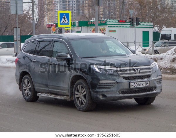 Novosibirsk, Russia - Februyary 24 2021: private\
all-wheel drive black metallic japanese family midsize SUV Honda\
Pilot, new car business class big crossover from Japan driving on\
snow winter street