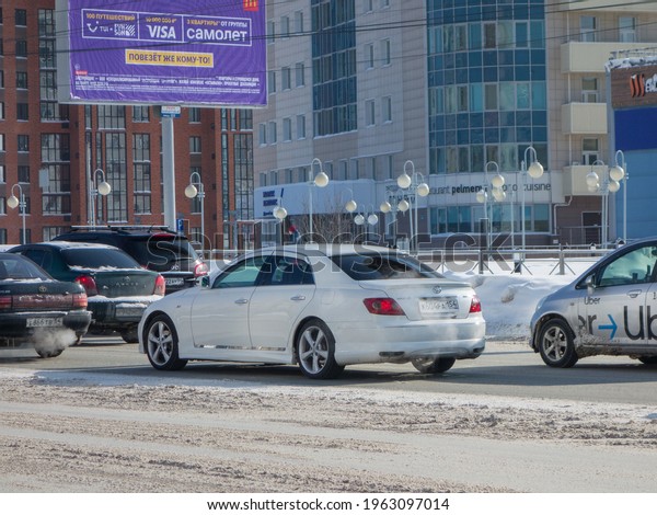 Novosibirsk, Russia - march 02 2021: private white\
pearl metallic old japanese RWD rear wheel drive car Toyota Mark X\
GRX120, midsize sport sedan from Japan from 2000s driving on winter\
snow street