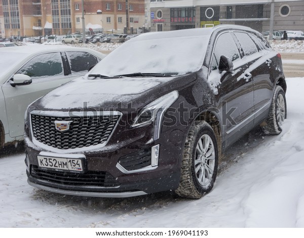 Novosibirsk, Russia - March 05 2021: private all-wheel\
drive brown black metallic color north american new car SUV\
Cadillac XT5, USDM US-spec crossover exported from USA parking on\
snow winter street\
