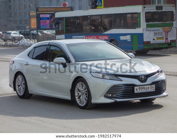 Novosibirsk, Russia - march 15 2021: private white\
pearl metallic japanese fwd front wheel drive car new Toyota Camry,\
midsize premium sedan made in Japan export import driving dirty\
urban street