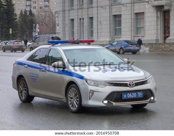 Novosibirsk, Russia - march 26 2021: private\
silver gray metallic special color japanese midsize premium sedan\
Toyota Camry Exclusive facelift XV50, road police car driving on\
spring wet sleet\
street
