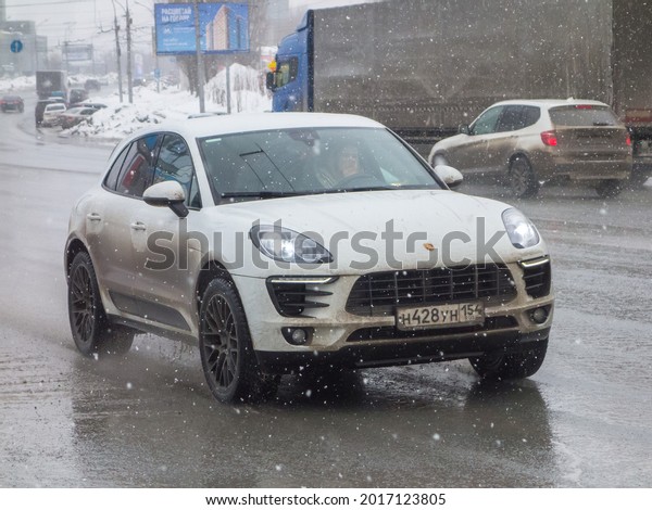 Novosibirsk, Russia - march 29 2021: private awd\
all-wheel 4wd 4x4 drive white metallic color sport coupe crossover\
Porsche Macan (95B) luxury car made in Germany SUV 4wd driving on\
wet broad street