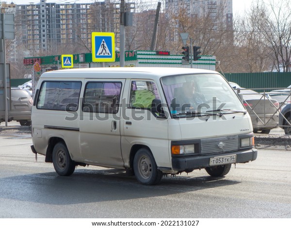 Novosibirsk, Russia - march 31 2021: private white\
color cargo passenger japanese min van bus car 80s Nissan Urvan\
EU-Spec LHD, minibus export import made in Japan driving on dirty\
broad urban street