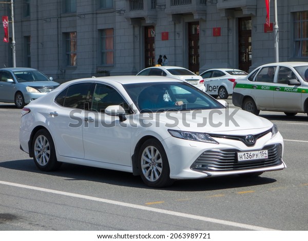 Novosibirsk, Russia, May 04 2021: private snow-white\
metallic color new japanese popular reliable midsize sedan Toyota\
Camry XV70 bestseller business class car drive on summer sunny city\
urban street 