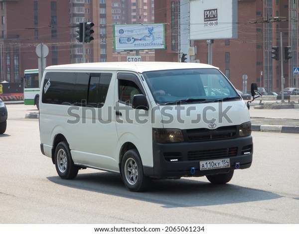 Novosibirsk, Russia, may 13 2021: private white\
metallic color cargo passenger japanese minivan car Toyota HiAce\
Regius Ace low roof, delivery van mini bus made in Japan drive on\
sunny city street
