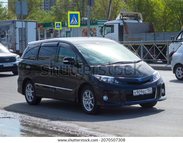 Novosibirsk, Russia, may 14 2021: private rare\
black metallic color passenger japanese minivan car Toyota Estima\
(Previa) Aeras Hybrid, mini van bus export import made in Japan\
drive on sunny\
street