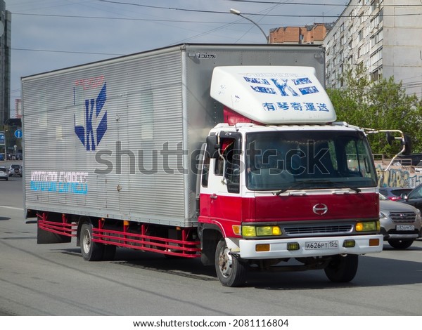 Novosibirsk, Russia, may 17 2021:  white red metallic\
color japanese aluminum box truck car chassis 90s Hino Ranger\
owned, old popular small cargo mini truck made in Japan drive on\
sunny urban street\
