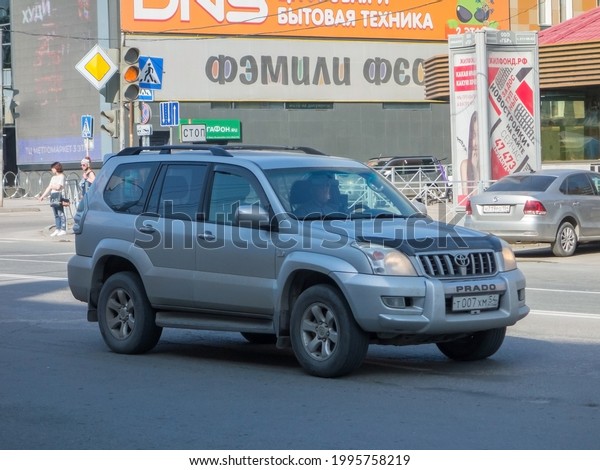 Novosibirsk, Russia - May 26 2021: private all-wheel\
drive 4x4 silver gray metallic color japanese frame SUV old 2000s\
00s Toyota Land Cruiser Prado, car crossover driving urban city\
summer street \
