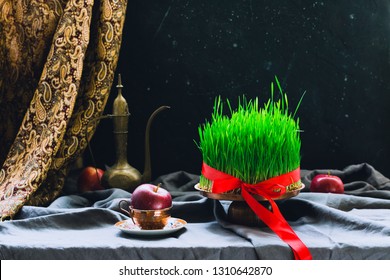 Novruz setting in Azerbaijan with black tea in armudu pear shape drinking glass with green wheat grass semeni with red ribbon for celebration. Spring equinox, Persian Nowruz greeting card copy space 