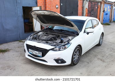 Novyy Urengoy, Russia - August 1, 2021: White Compact Car Mazda 3 With The Opened Bonnet Near The Garage.