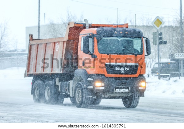 Novyy Urengoy,\
Russia - January 11, 2020: Orange dump truck MAN TGS in the city\
street during a heavy\
snowfall.