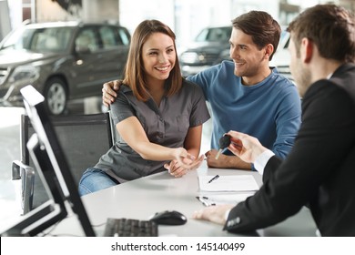 Now her dream comes true. Car salesman giving the key of the new car to the young attractive owners