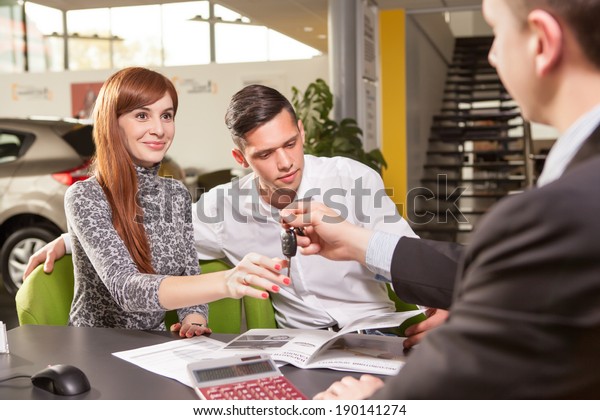 Now her dream comes true. Car
salesman giving the key of the new car to the young attractive
owners