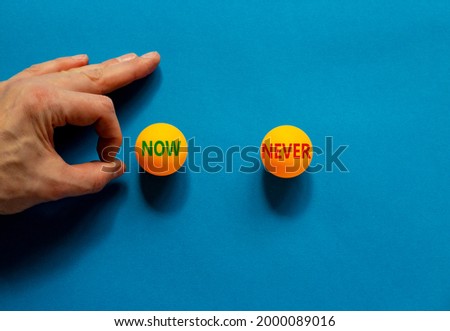 Now or never symbol. Male hand is about to flick the ball. Orange table tennis balls with words now never. Beautiful blue background. Business, now or never concept.