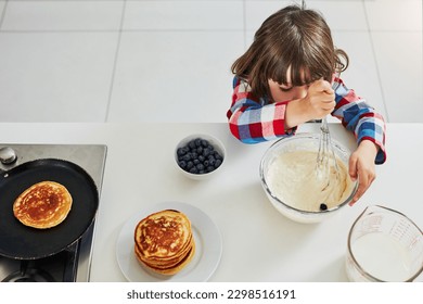 Now time to mix it. High angle shot of an adorable little boy making pancakes in the kitchen at home.