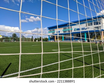 Noyabrsk, Russia - July 17 2022: View Of The Noyabrsky Sports Stadium And Football Field With Bright Green Grass Through The Safety Net. The Family Plays Football On A Summer Day. Selective Focus.