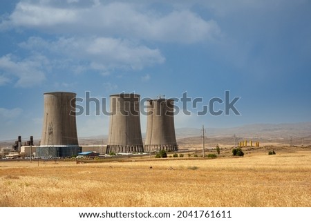 Nuclear power plant cooling towers, big chimneys beside Wheat field with partly cloudy sky in Kurdistan province, iran