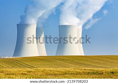 NUCLEAR POWER PLANT COOLING TOWERS SMOKING IN THE YELLOW AGRICULTURAL FIELD AGAINST THE BLUE SKY, ATOMIC ENERGY AS ALTERNATIVE ENERGY SOURCE, ELECTRICITY PRODUCTION CONCEPT