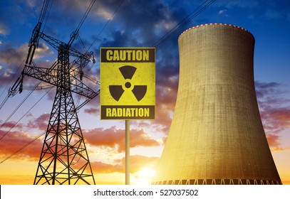 Nuclear Power Plant With Radioactivity Warning Symbol And Electricity Pylon At Sunset.