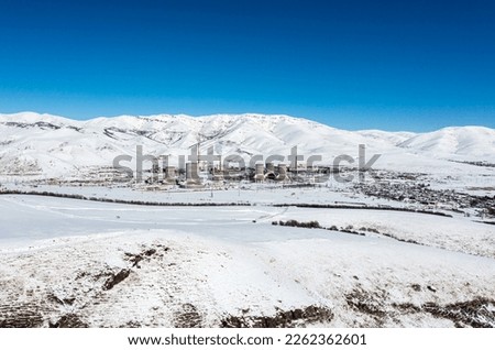 nuclear powerplant on the field between snowy mountains in winter time with smokey pipes