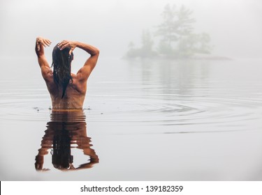 Nude Back Of Middle Aged Caucasian Woman Bathing  And Washing Hair In Maine Lake On A Foggy Summer Morning.