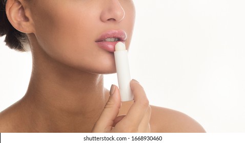 Nude Makeup Concept. Close Up Of Woman Applying Lip Balm Stick Isolated Over White Studio Wall