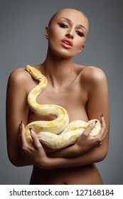 nude portrait of lovely young woman covering her breast with albino python over gray background
