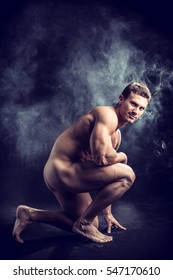 Nude Profile Of Young Muscle Man Crouching In Fog In Studio With Black Background