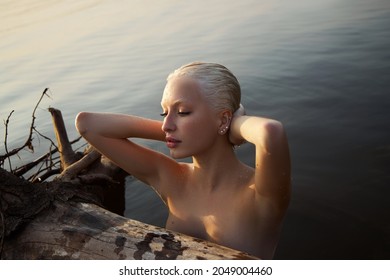 Nude sexy woman in water at sunset. Beautiful blonde woman with short wet hair and big breasts, art portrait in sea