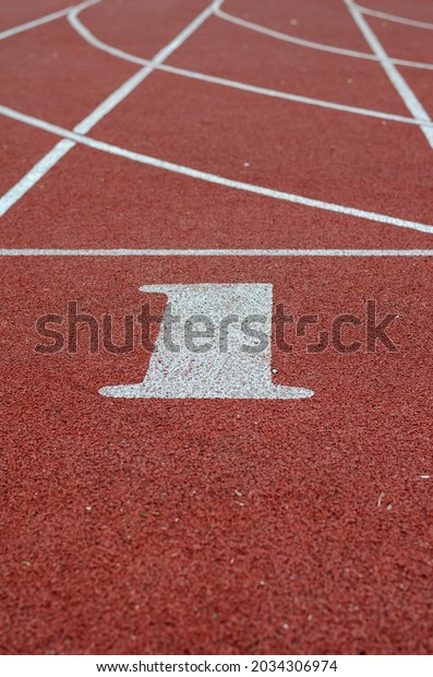 Number 1 on\
the start line for running. Red jogging tracks at the stadium.\
Sports, active lifestyle. Selective\
focus.