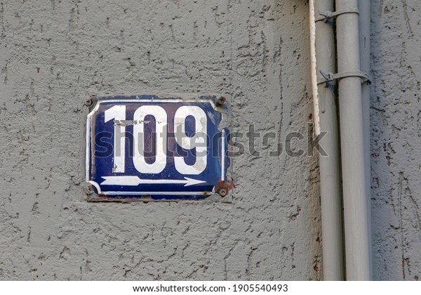 Number 109, the number of houses, apartments,\
streets. The white number on a blue metal plate, house number one\
hundred and nine (109) on a rough\
wall.
